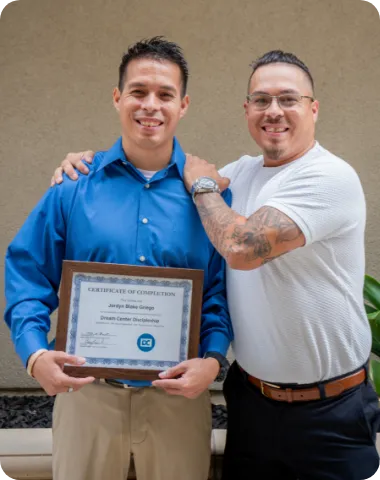 Two men smiling, one with his hand on the other’s shoulder holding a certificate.