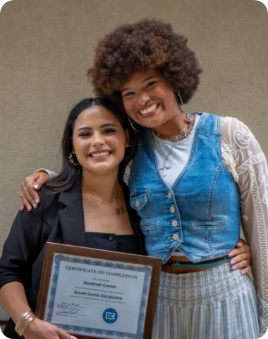 Two women smiling and posing together, one holding a framed certificate.