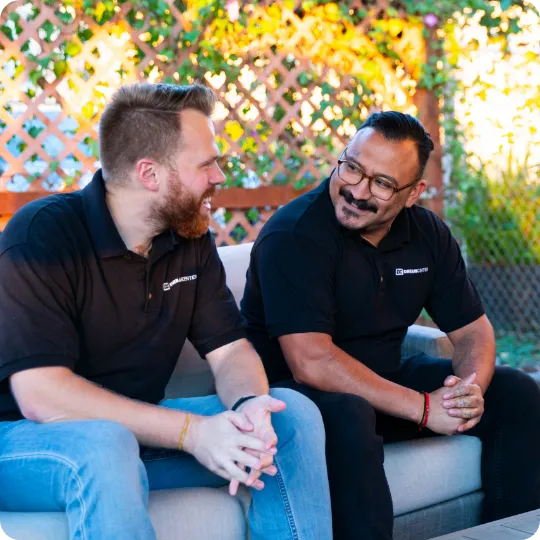 Two men sitting on an outdoor couch, smiling and talking while wearing matching black Dream Center shirts.