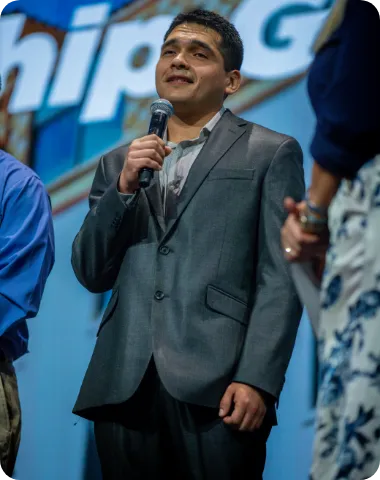 Man in a suit speaking on stage while holding a microphone.