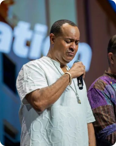 A man holding a microphone with his eyes closed in prayer during a ceremony.